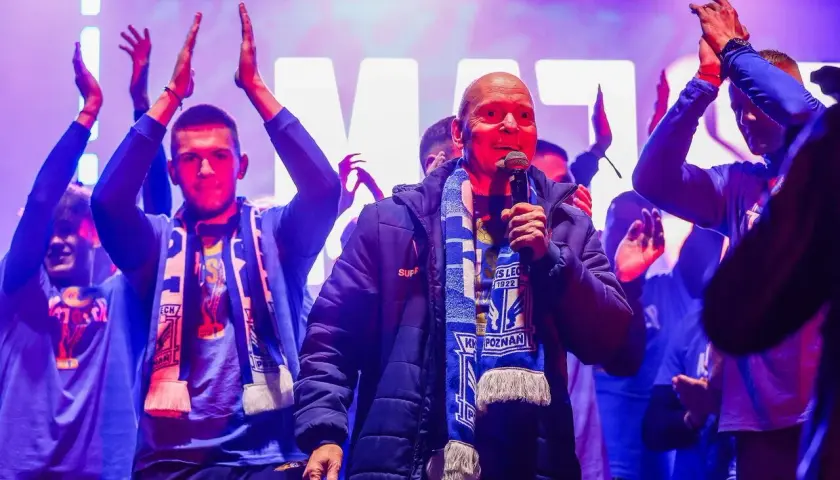 Mężczyzna z mikrofonem, otoczony przez młodych ludzi w szalikach, świętuje sukces jako mistrz polski ekstraklasa.