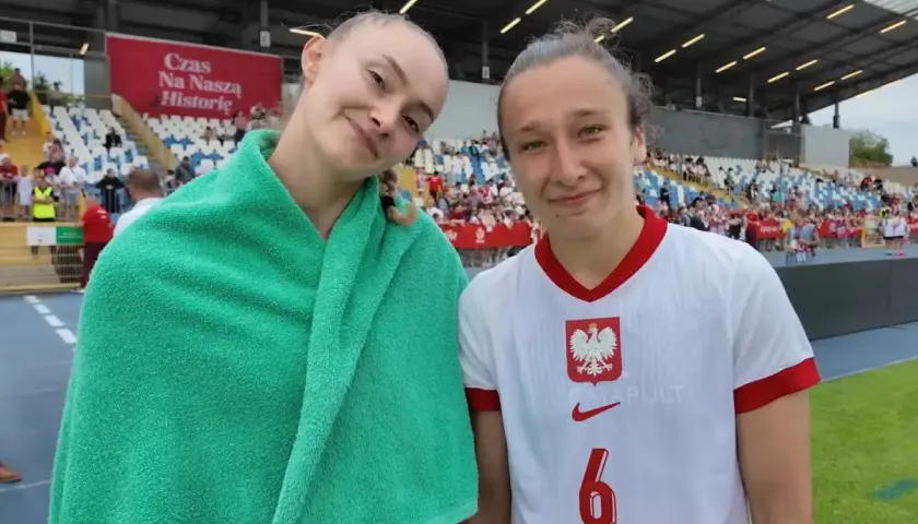Dwie młode piłkarki w strojach reprezentacji Polski na tle trybun stadionu.