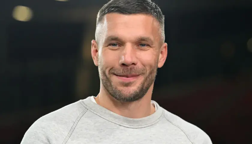 Uśmiechnięty Lukas Podolski w szarej bluzie. Jego majątek budowany latami kariery piłkarskiej i biznesów.