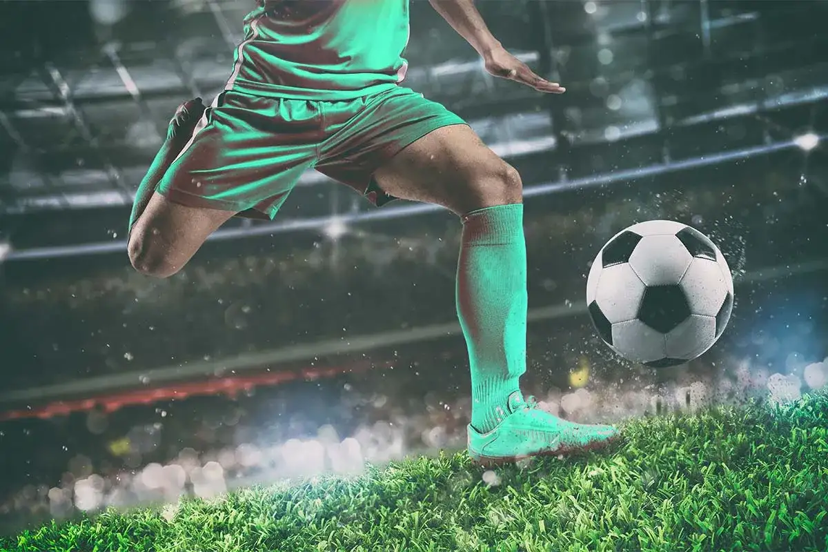 Piłkarz w zielonym stroju drybluje piłką na tle stadionu. To obraz, który przywołuje ducha legend piłki nożnej.