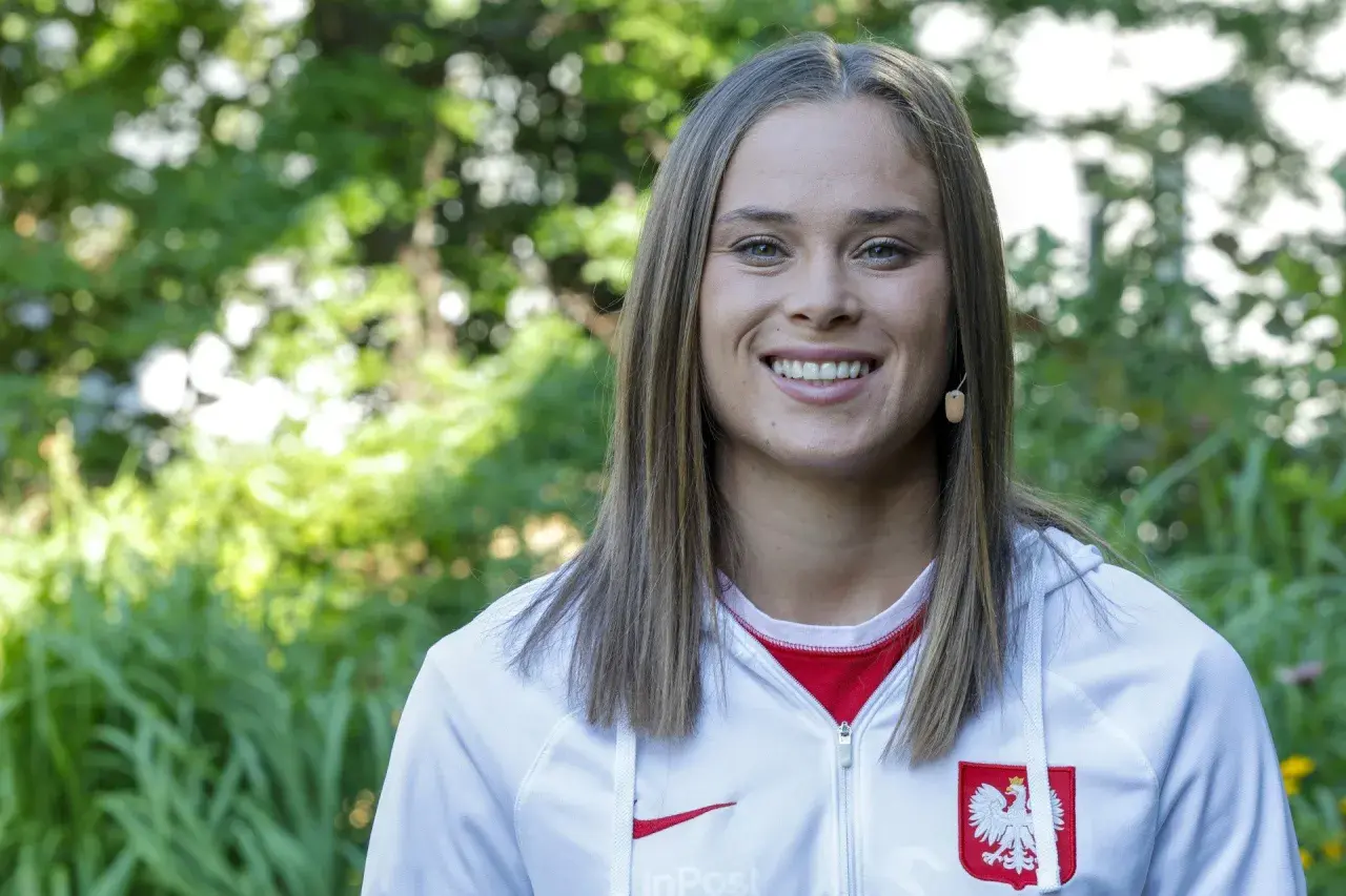 Uśmiechnięta Ewa Pajor w stroju reprezentacyjnym, symbol polskiego sportu. Jej zarobki budzą zainteresowanie, ale talent i determinacja są bezcenne.