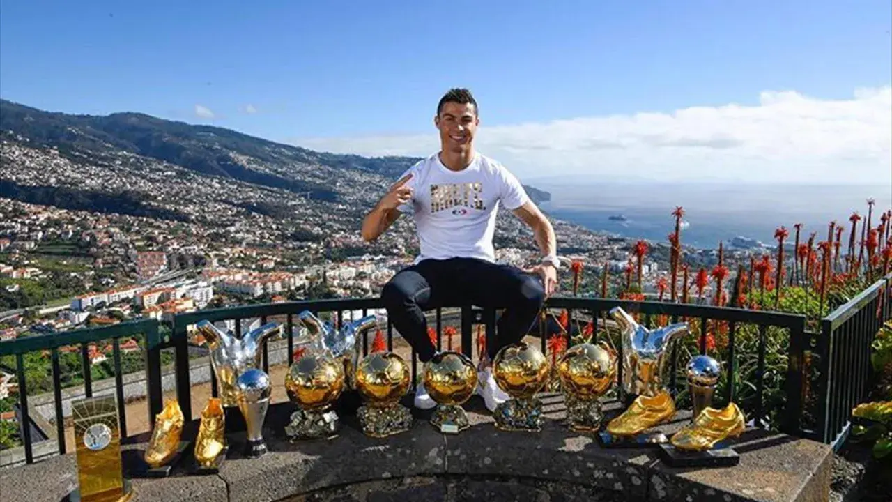 Cristiano Ronaldo z pięcioma złotymi piłkami, symbolizującymi jego sukcesy.