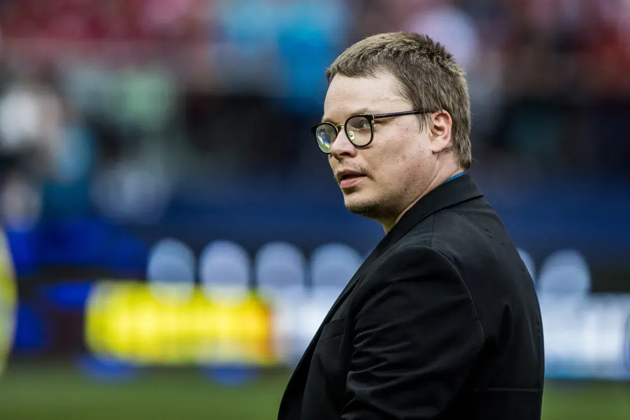 Jarosław Królewski w okularach, w czarnym garniturze, na tle stadionu.