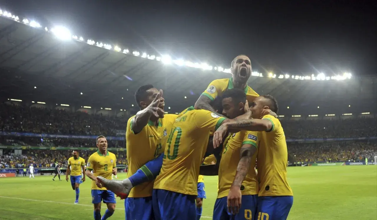 Piłkarze Brazylii świętują zwycięstwo nad Argentyną. Stadion wypełniony kibicami, nocne światła oświetlają murawę.