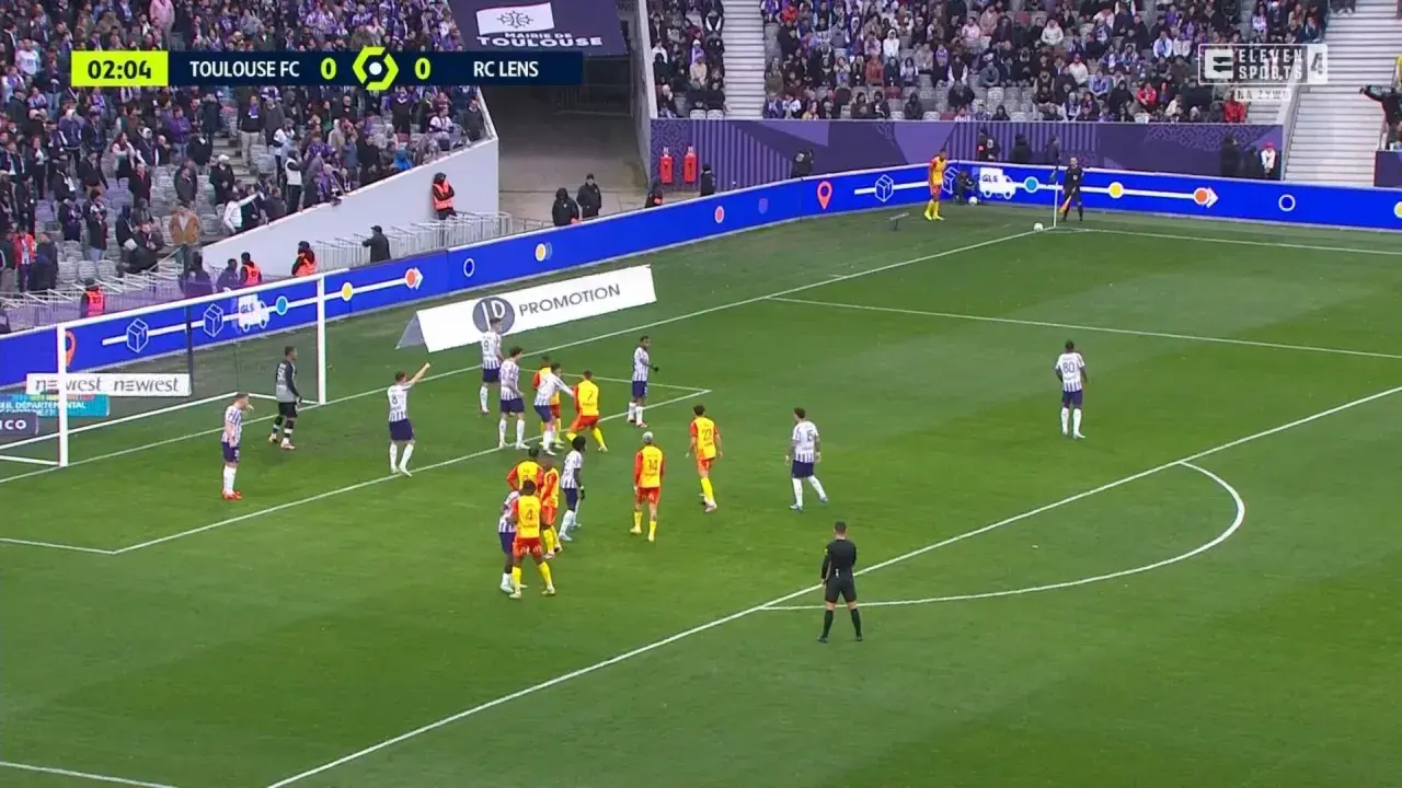 Mecz Toulouse FC - RC Lens. Piłkarze w białych i żółtych strojach szykują się do akcji pod bramką.