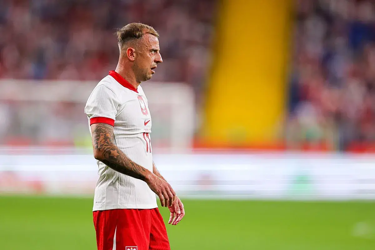 Piłkarz Kamil Grosicki w białej koszulce i czerwonych spodenkach, z tatuażami na ramieniu. Jego majątek budowany latami kariery.