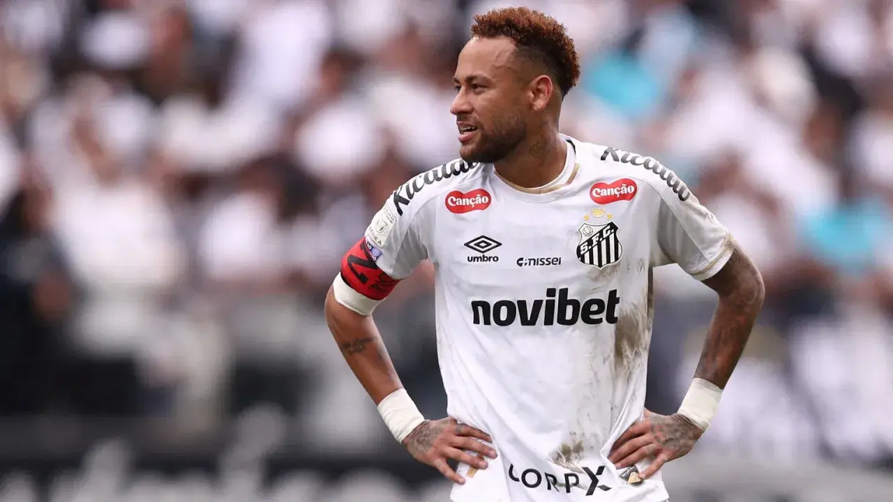 Neymar w białej koszulce Santos FC, z opaską kapitana na ramieniu, na tle trybun.