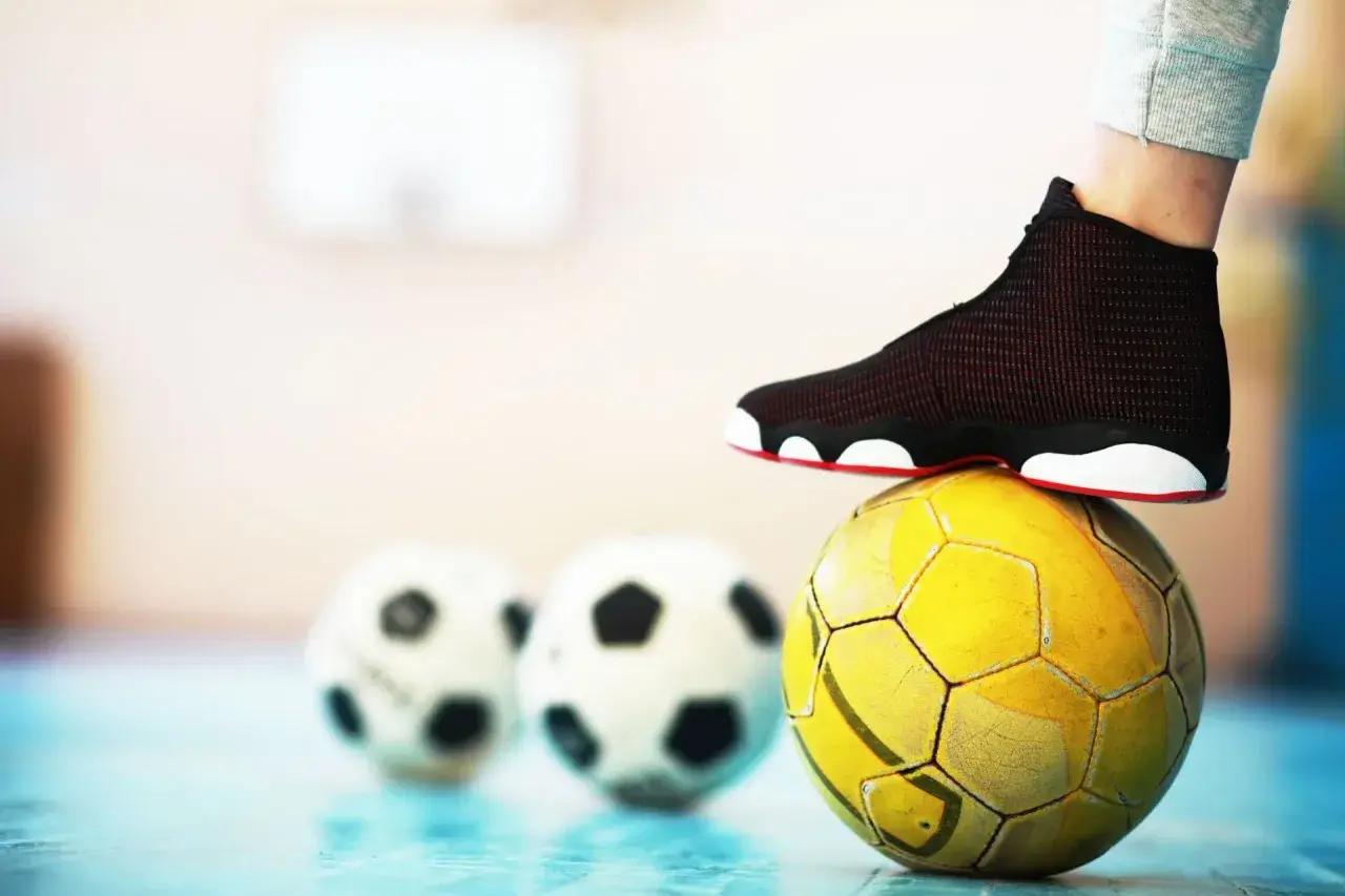 Stopa na żółtej piłce, w tle dwie białe. To może być początek przygody z futsalem.