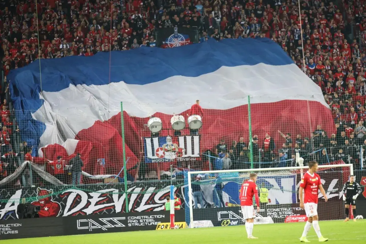 Oprawa meczu Ruch Chorzów – Wisła Kraków. Ogromna flaga w barwach biało-czerwono-niebieskich zakrywa trybuny, a pod nią bębny i kibice.