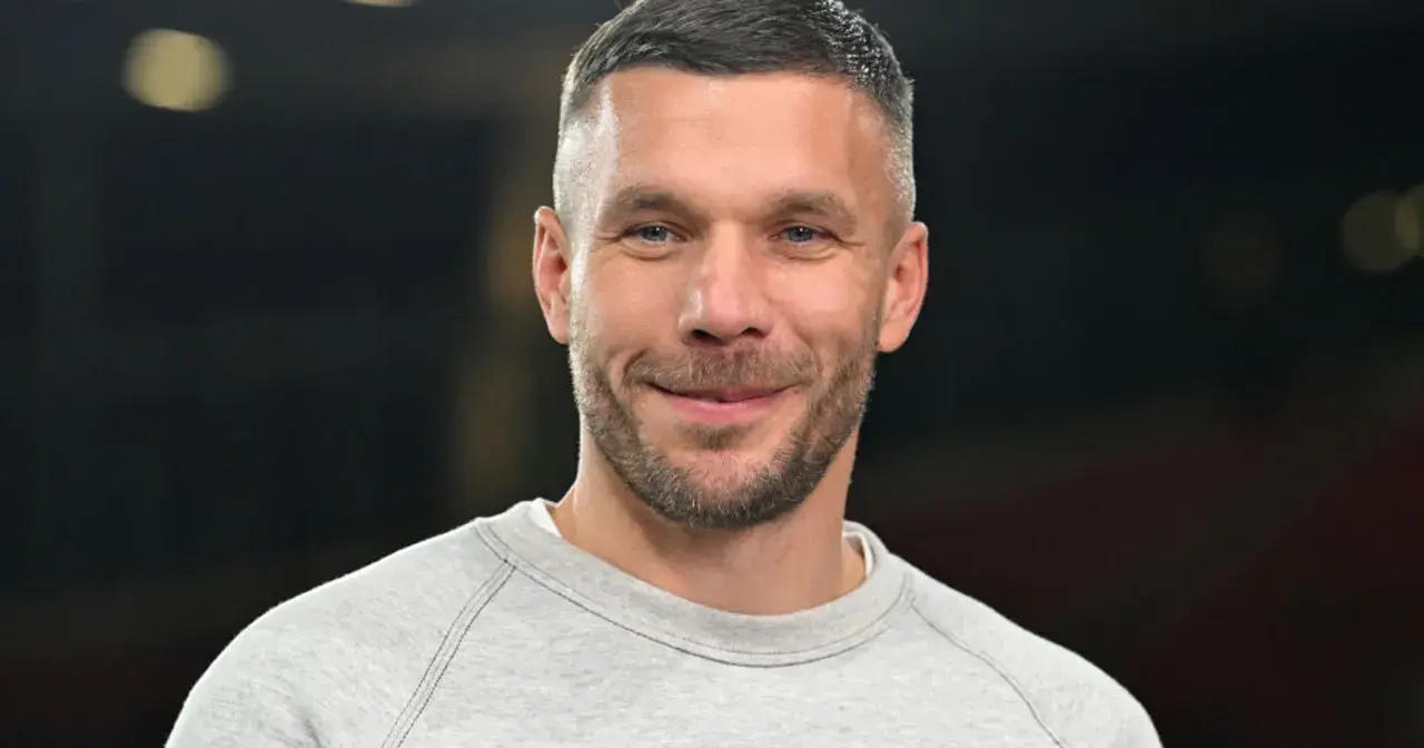 Uśmiechnięty Lukas Podolski w szarej bluzie. Jego majątek budowany latami kariery piłkarskiej i biznesów.
