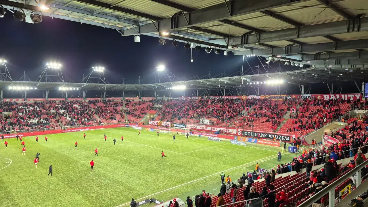 Stadion Widzewa Łódź wypełniony kibicami. Na murawie zawodnicy, w tle banery 