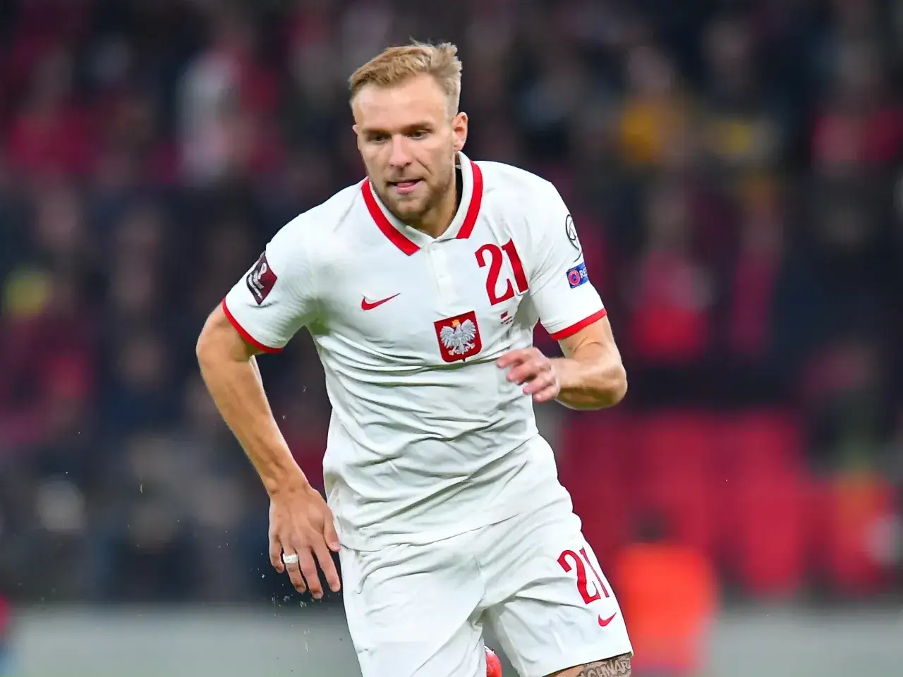 Piłkarz w białej koszulce z orłem i numerem 21, gotowy do gry. Gdzie gra puchacz? Na boisku!