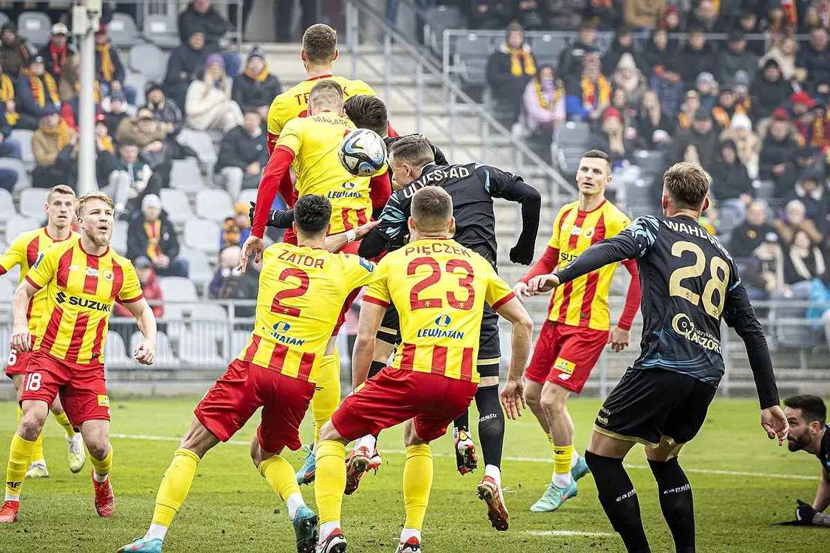 Intensywny przebieg: pogoń szczecin – korona kielce. Piłkarze walczą o piłkę w powietrzu, kibice na trybunach.