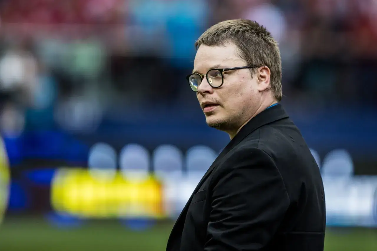 Jarosław Królewski w okularach, w czarnym garniturze, na tle stadionu.