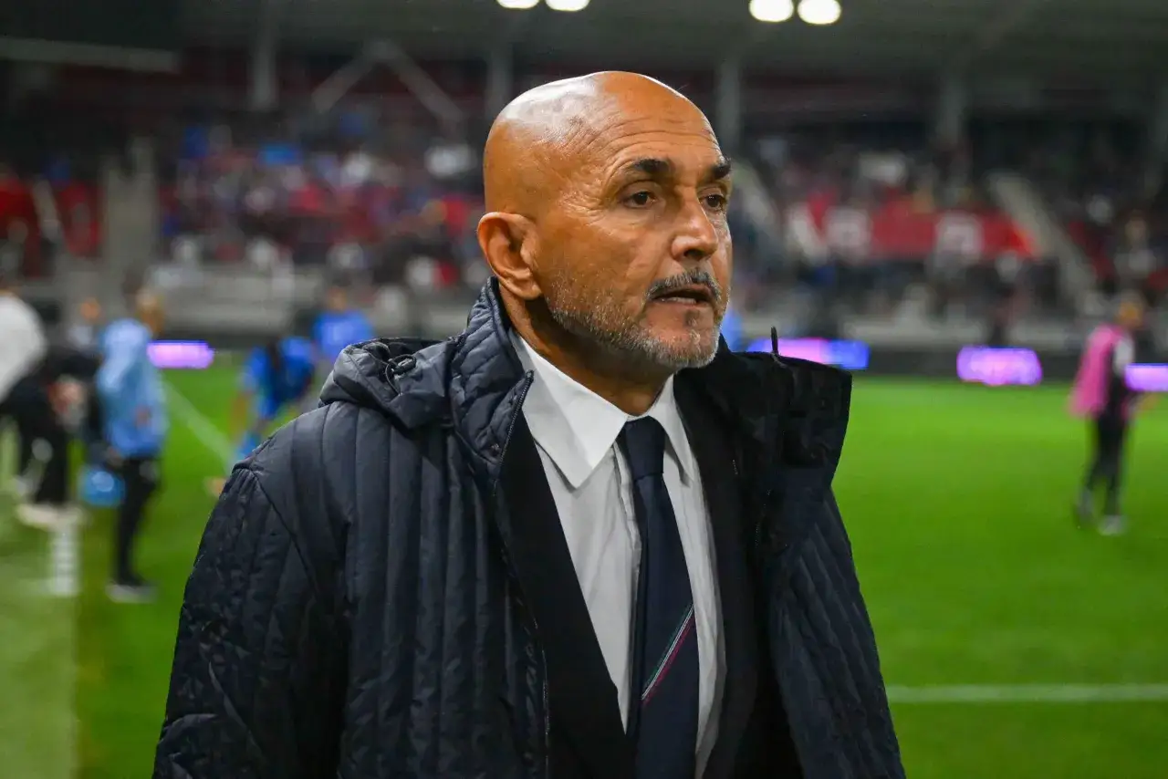 Łysy mężczyzna z brodą, ubrany w białą koszulę i granatowy krawat, w ciemnej kurtce. To trener Juventusu, skupiony na boisku.