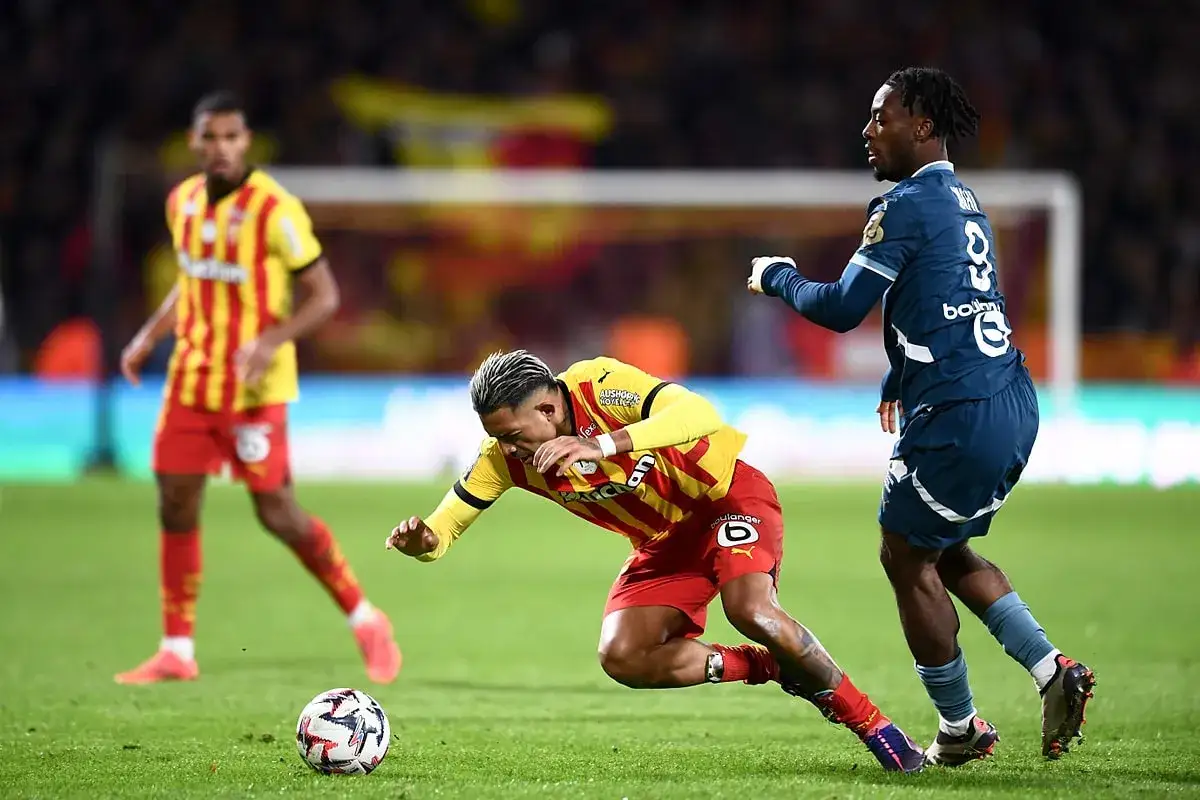 Piłkarz RC Lens w żółto-czerwonej koszulce walczy o piłkę ze zawodnikiem Stade Rennais.