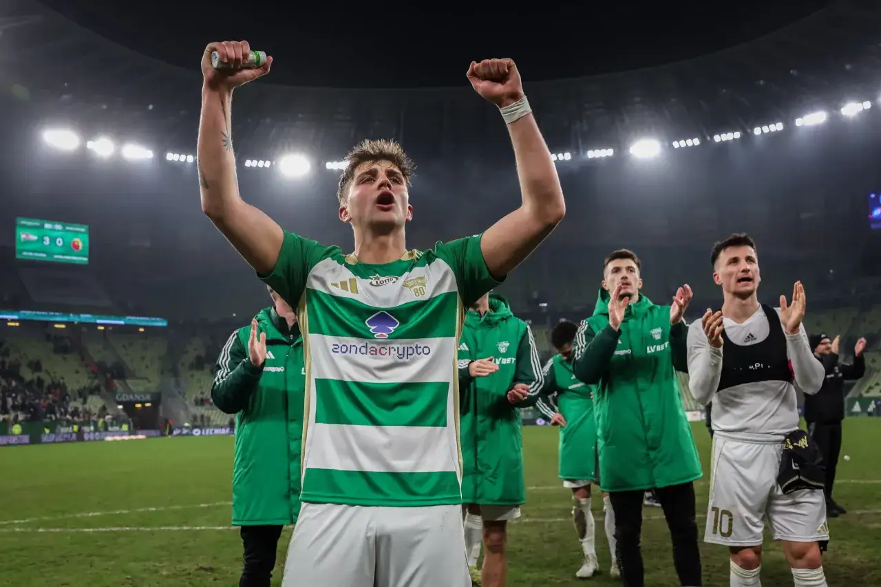 Piłkarz Lechii Gdańsk z podniesionymi rękami świętuje zwycięstwo nad Pogonią Szczecin. Wynik 3:0 widoczny na tablicy.