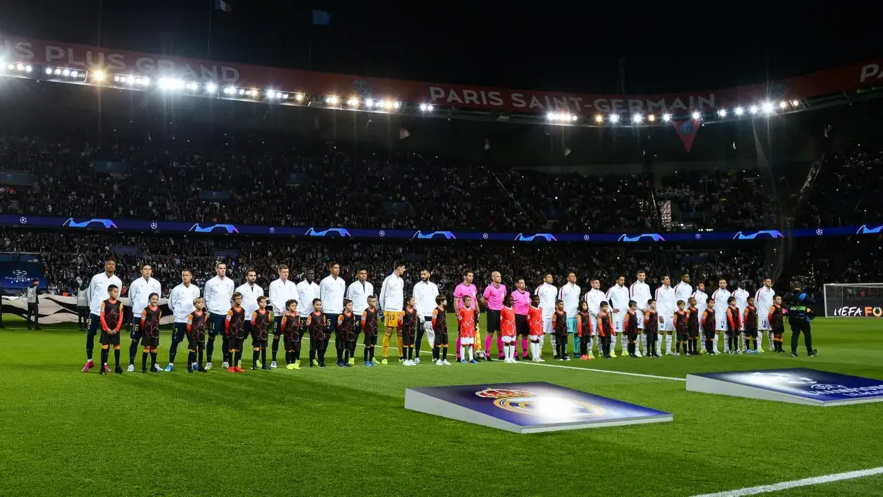 Piłkarze i dzieci stoją na murawie stadionu przed meczem, słychać hymn Ligi Mistrzów.