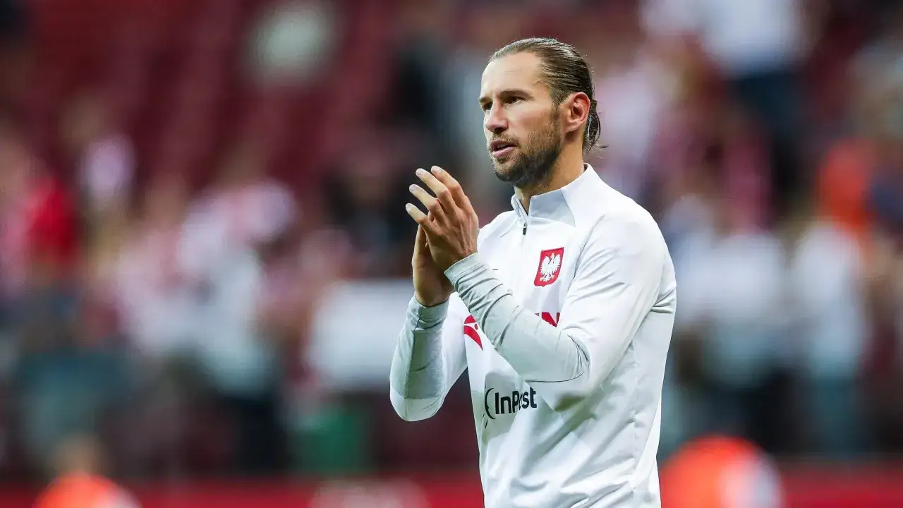 Piłkarz w białej koszulce z orłem na piersi, z długimi włosami spiętymi w kucyk, klaszcze. Czy to Krychowiak, gdzie gra?