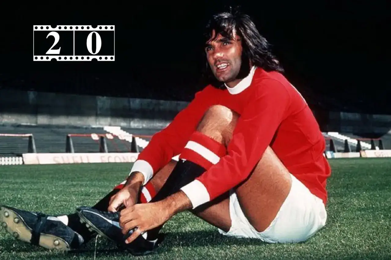 George Best, jedna z legend piłki nożnej, w czerwonej koszulce Manchesteru United, siedzi na murawie, poprawiając but.