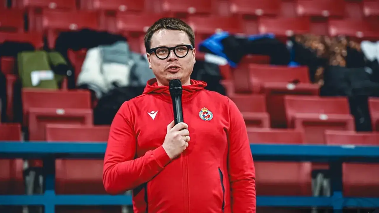 Właściciel Wisły Kraków w czerwonej bluzie z kapturem i mikrofonem przemawia na tle pustych trybun stadionu.
