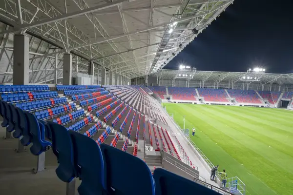 Puste trybuny stadionu Odra Opole w kolorach niebieskim i czerwonym, oświetlone nocą.